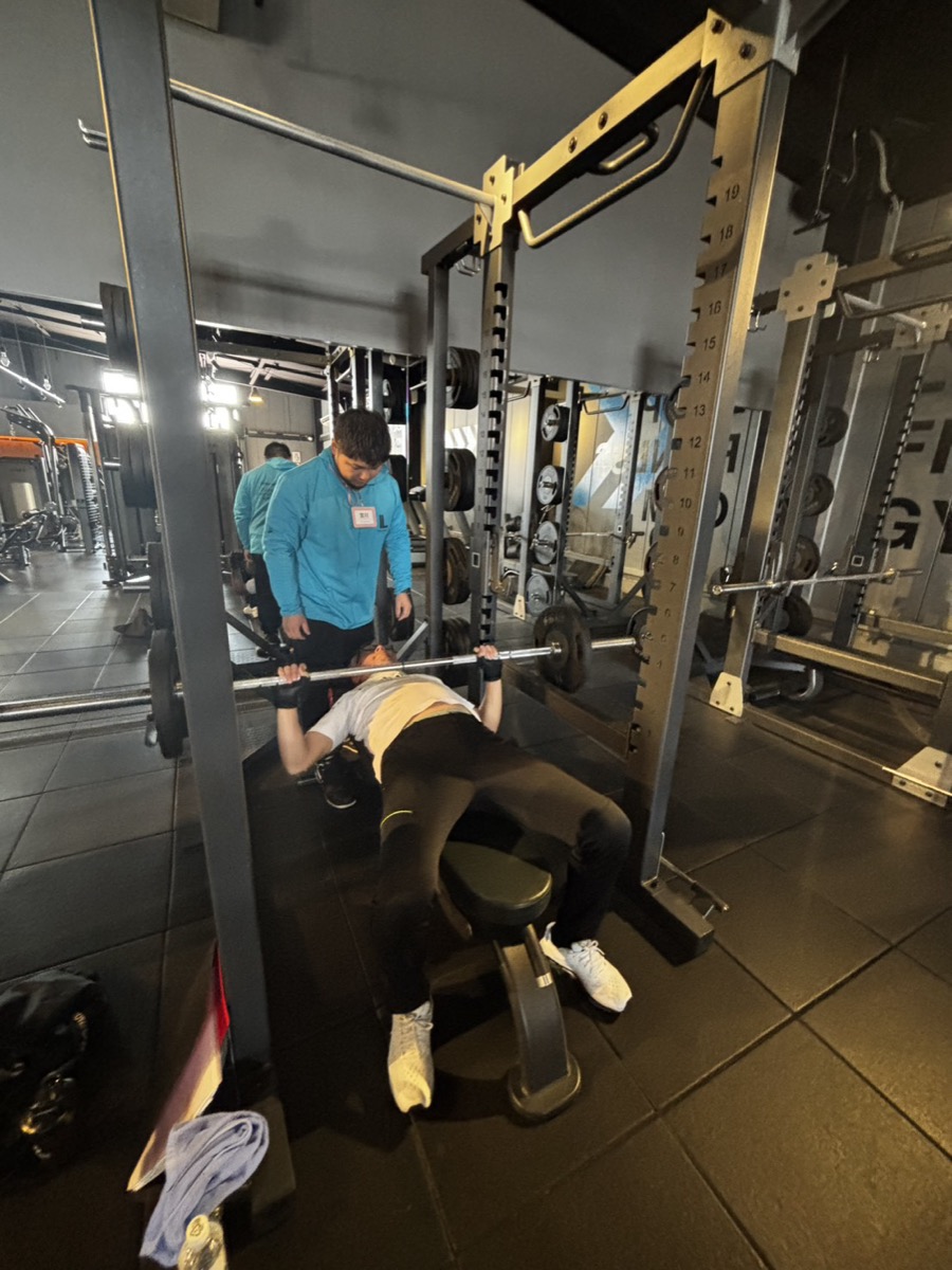 トレーナーがベンチプレスの補助をしている様子